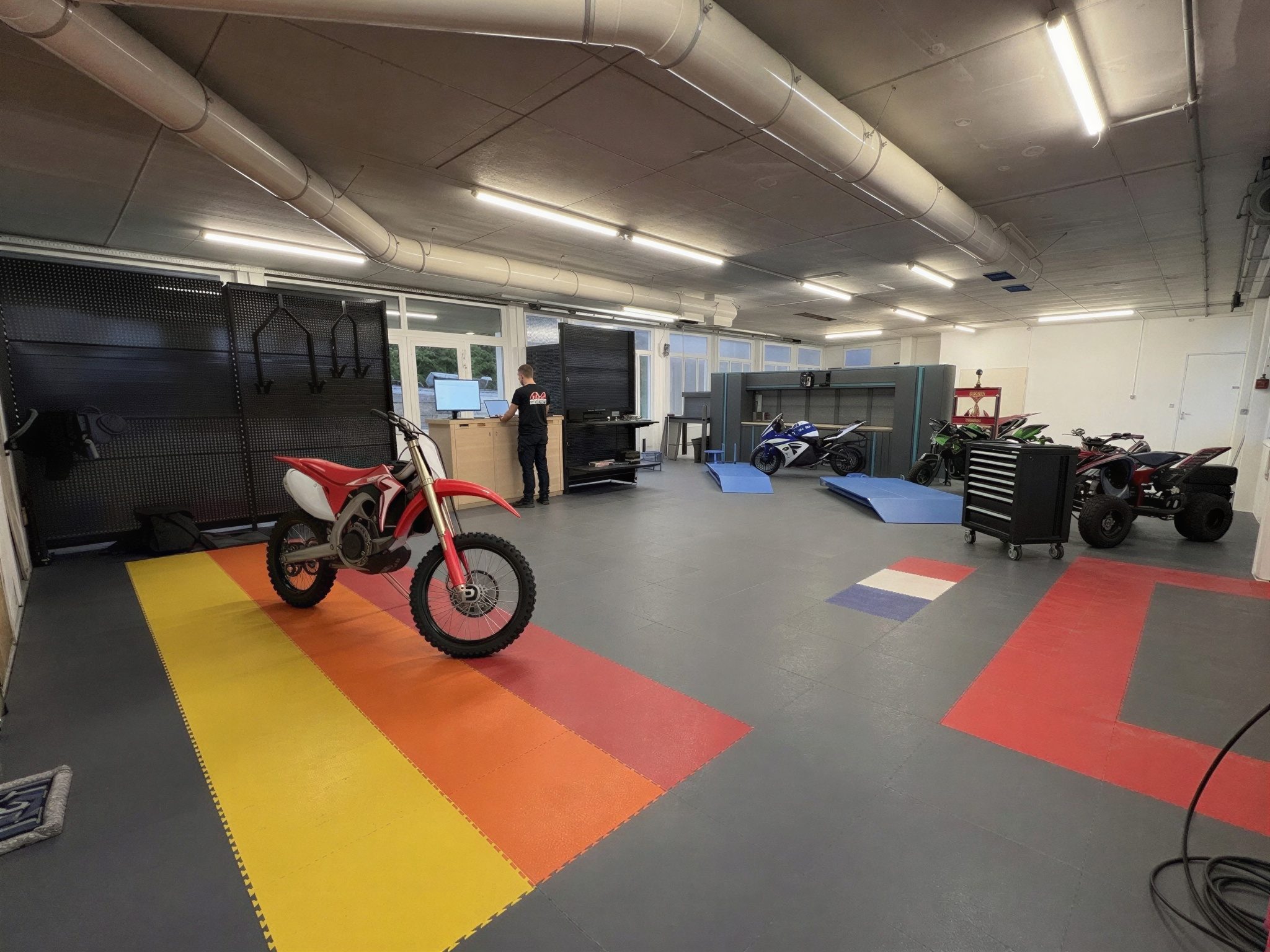 Atelier AJ Moto à Frambouhans : sol en dalles modulaires, motos cross et de route, quads et comptoir d’accueil