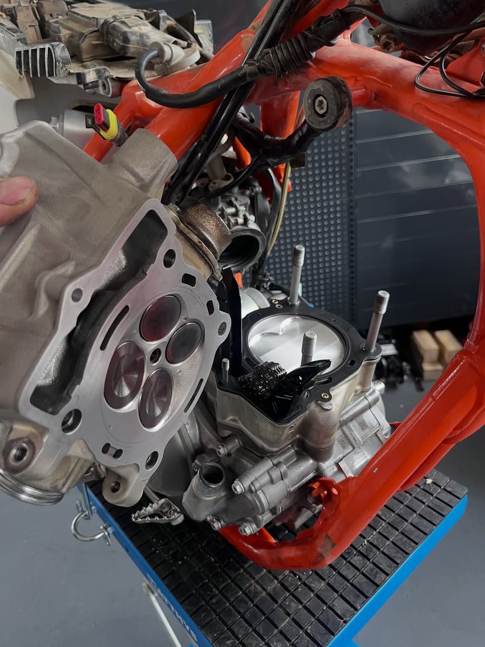 Moteur de moto cross ouvert dans son cadre, culasse déposée à la main au-dessus du haut moteur