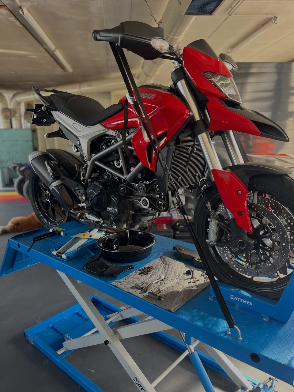 Ducati Hypermotard sur le pont élévateur de l’atelier AJ Moto, bac de vidange sous le moteur